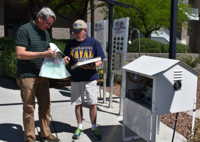 Two people stand next to a monitoring station flipping through information.
