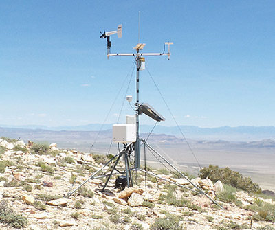 A monitoring station is placed on the summit of a mountain with the valley outstretched in the background. 