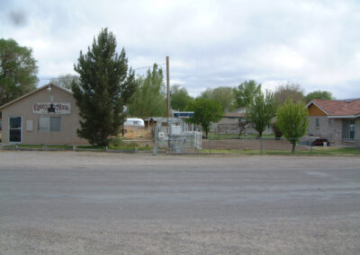 Single-story homes with trees and a fenced utility area are visible across a paved road under a cloudy sky.