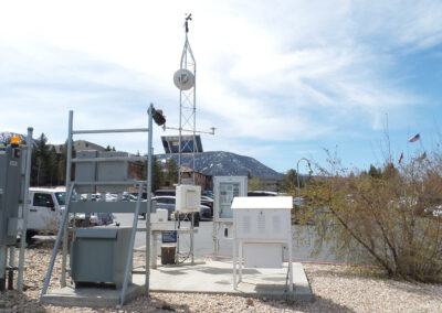 Weather monitoring station with various instruments and sensors, a tall tower with anemometer, and a mountain in the background under a partly cloudy sky.