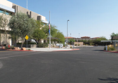 A paved road curves past a modern building, trees, and a flag at half-mast under a clear blue sky.
